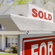 Sold sign in front of a residential home with a blurred background, representing the sale of a home and potential tax implications of real estate transactions.
