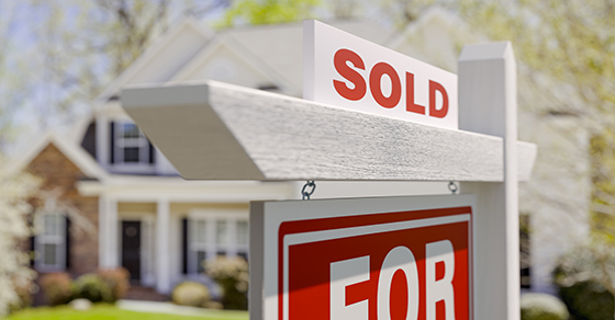 Sold sign in front of a residential home with a blurred background, representing the sale of a home and potential tax implications of real estate transactions.