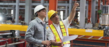 Two workers in hard hats reviewing plans in a manufacturing facility, representing repair vs. capital improvement decisions and tax preparation in Bel Air, MD from Weyrich, Cronin & Sorra.