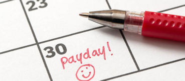 Calendar marked "Payday!" with a smiley face beside a red pen, representing payroll tax compliance and accounting services from a CPA near Towson at Weyrich, Cronin & Sorra.