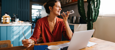Woman working remotely at a kitchen table with a laptop and phone, representing remote work state taxes and tax preparation for Elkton, MD residents from Weyrich, Cronin & Sorra.