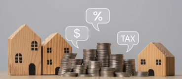 Wooden model houses beside stacks of coins with dollar, percent and tax speech bubbles, representing tax planning for real estate investors with an accountant in Baltimore at Weyrich, Cronin & Sorra.