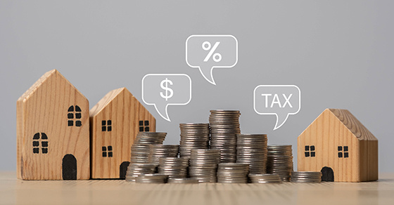 Wooden model houses beside stacks of coins with dollar, percent and tax speech bubbles, representing tax planning for real estate investors with an accountant in Baltimore at Weyrich, Cronin & Sorra.