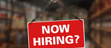 Red "Now Hiring?" sign hanging in a shop window, representing nonprofit hiring decisions and budgeting guidance from an accountant in Columbia, MD at Weyrich, Cronin & Sorra.